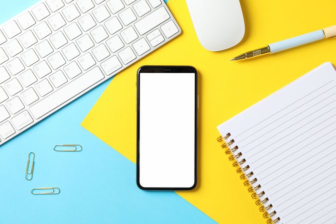 Workplace with phone with empty screen on color background, top view