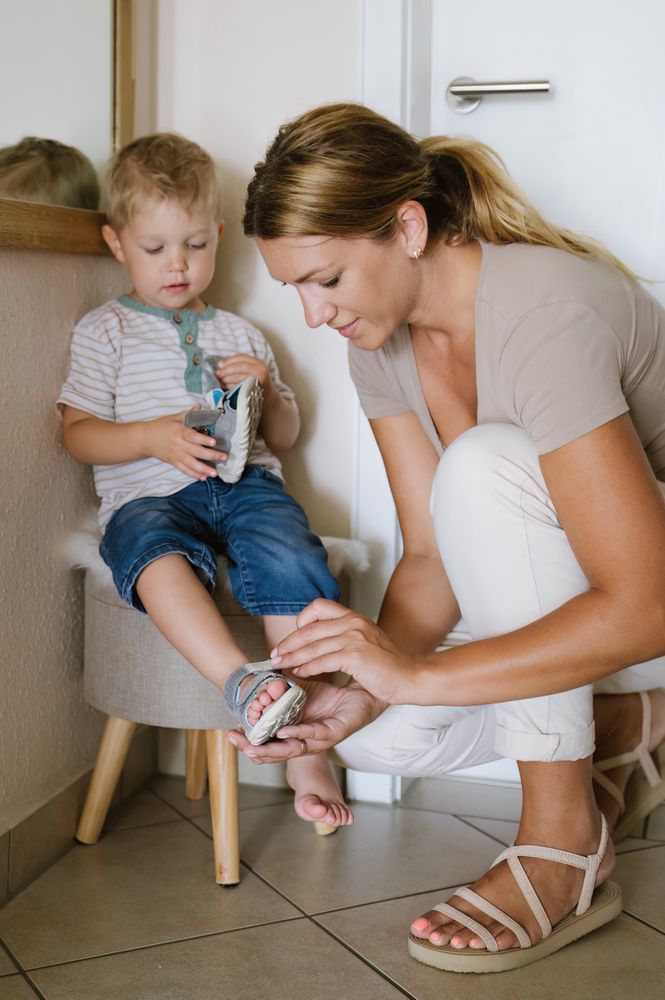 Mother sitting on floor and tying shoe belt on foot of kid son
