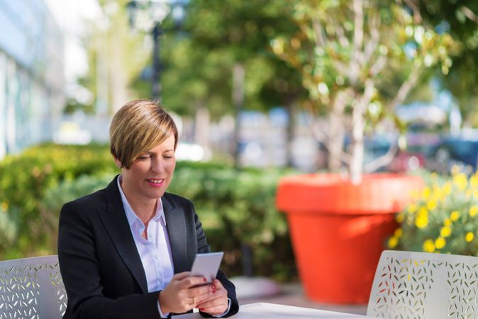 Smiling woman sitting on table outside checking phone