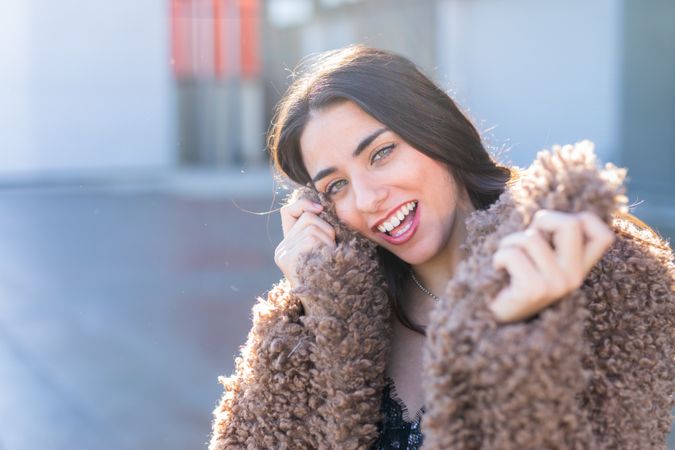 Cheerful woman wrapping in coat on street