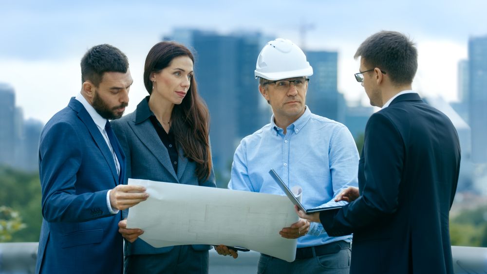 Team of Investors, Developers and Engineers Discuss Future of the Major Real Estate Project  with Major Contractor while Consulting Drafts and Plans.