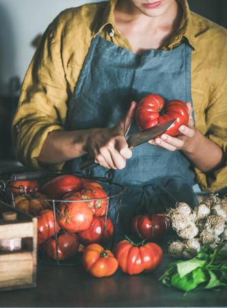 Woman in yellow halving large tomato with knife