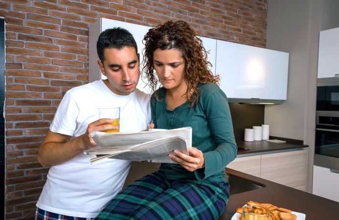 Couple in pajamas reading paper together in kitchen at breakfast time
