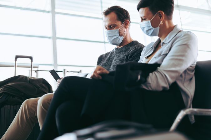 Couple sitting at airport with face mask using smart phone