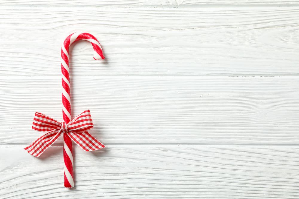 Sweet candy cane with bow on wooden background, space for text