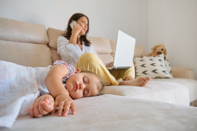 Sleeping daughter resting near mother with laptop and smartphone