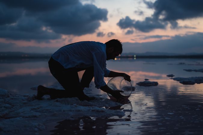 Focused man filling fish tank with water from sea in dusk