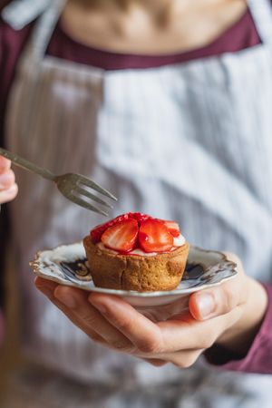 Baker holding strawberry custard tartlet on small dessert dish