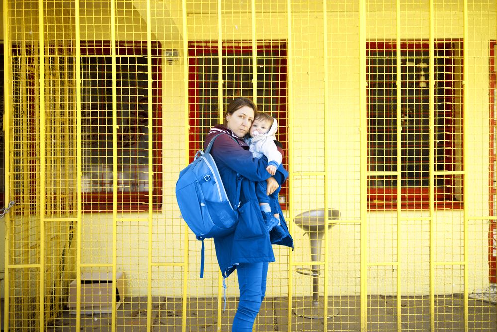 Woman in blue standing with her child in front of yellow wall