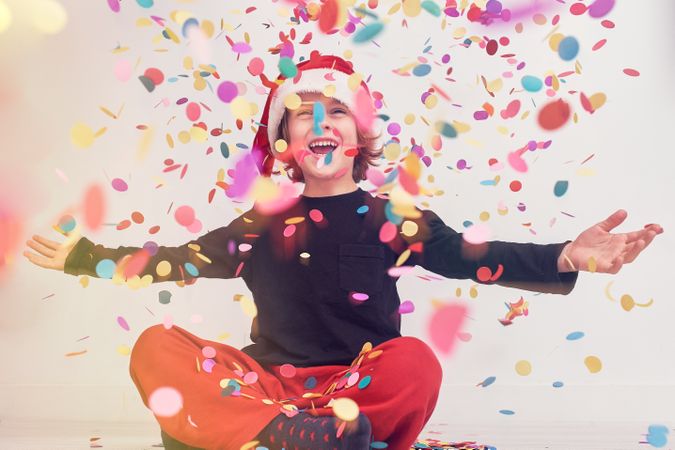 Joyful boy in Santa hat under falling confetti