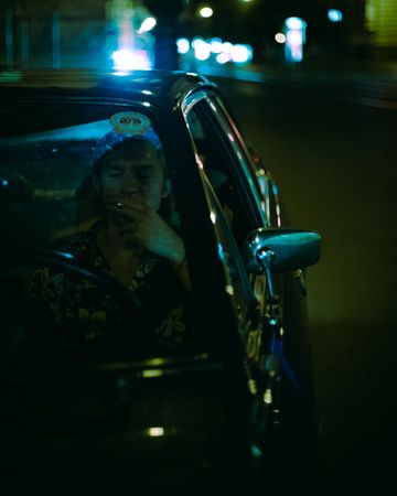 Young man smoking in an old car at night