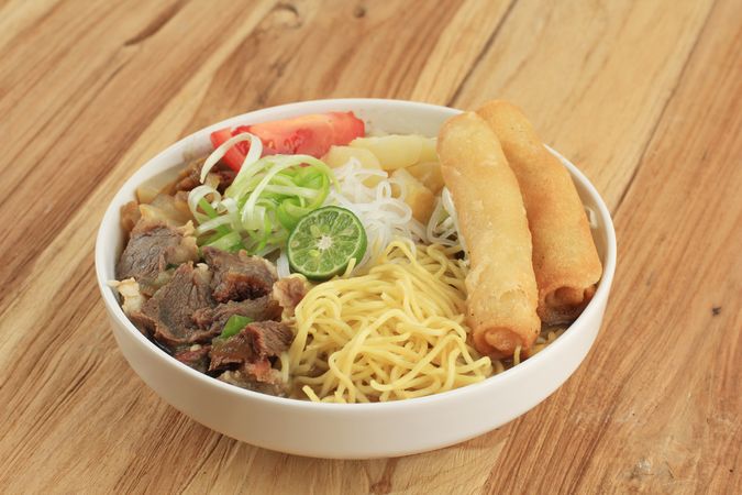 Bowl of Indonesian beef noodle soup with noodles, beef, spring roll, cabbage and tomato