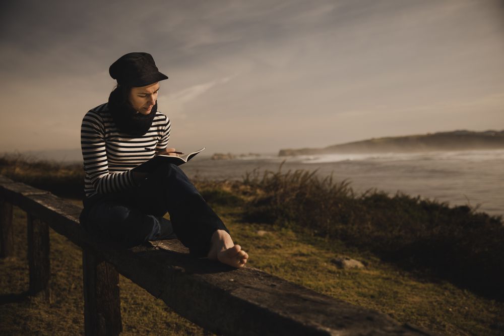 Woman writing in notebook and sitting on bench on shore near water