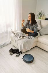 Smiling female sitting on sofa near sleeping dog and robotic vac