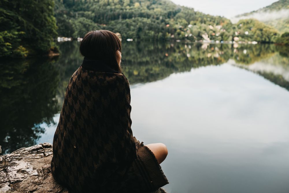 Woman sitting with blanket near lake and mountains