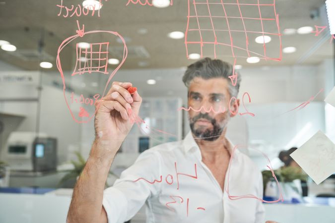 Serious bearded man working and writing on glass wall