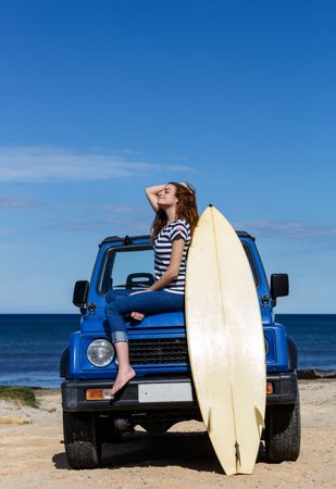 Woman sitting on top of a car with surfboard