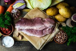 Ingredients for hearty soup with meat surrounding cutting board