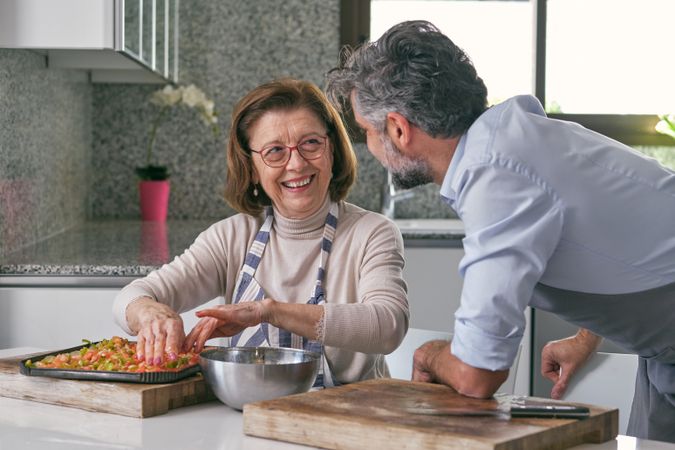Aged mother and son in aprons cooking together in kitchen