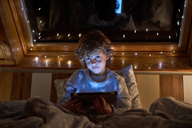 Boy playing on tablet in garland lit bedroom