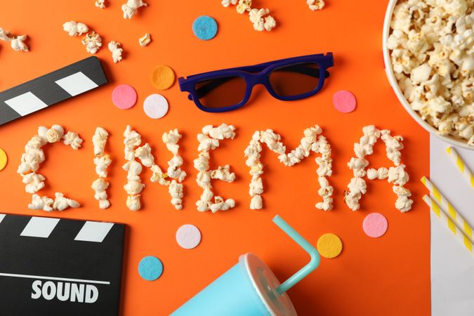 Word cinema laid out from popcorn and movie watch accessories on orange background