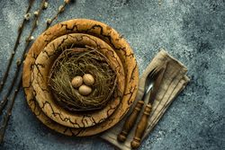 Top view of decorative eggs in delicate nest on rustic brown plate on table with space for text