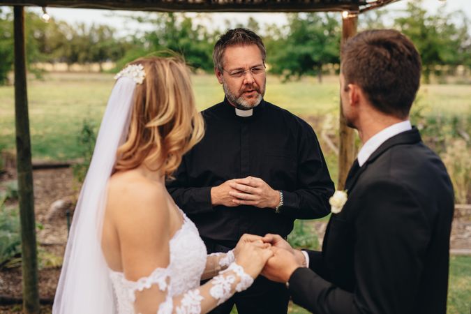 Male priest marries a couple in lovely outdoor wedding ceremony