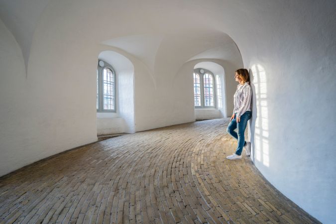 Casual woman leaning on wall in spacious gallery with windows