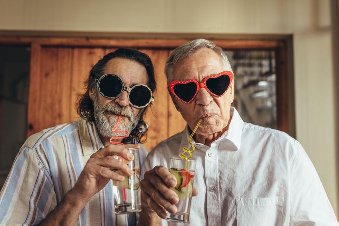 Two men wearing funny sunglasses drinking juice with straw