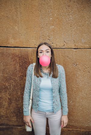 Young woman standing in front of stone wall blowing bubble gum