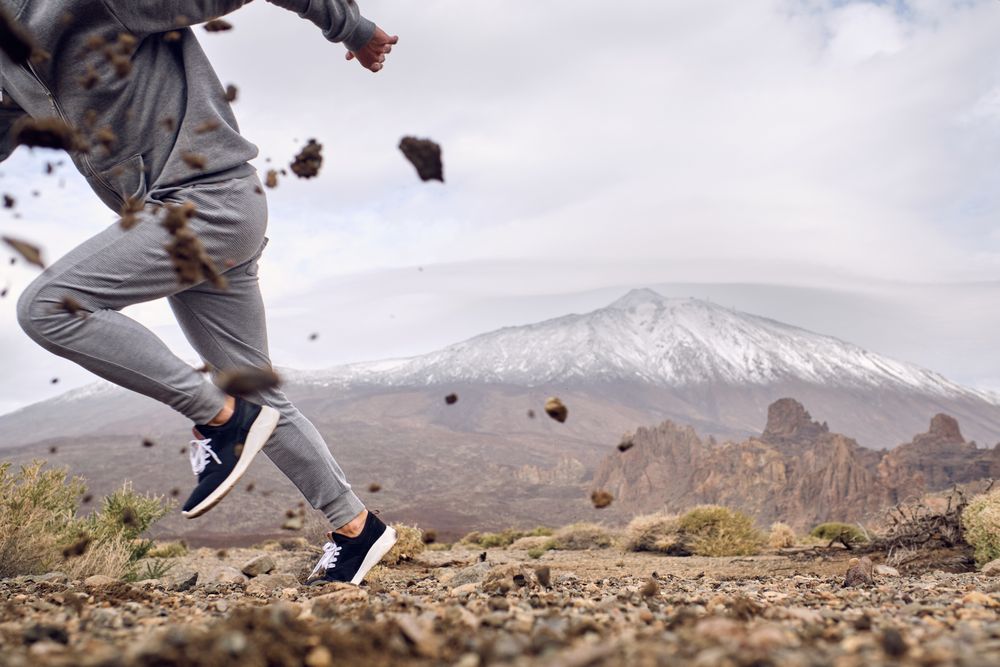 Crop man in activewear running on dirty terrain near mountains