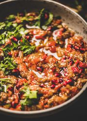 Eggplant dip with pomegranate and parsley garnish on wooden surface, close up