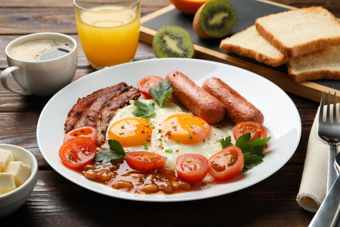 Two fried eggs sunny side up on plate with bacon and sausage on wooden table