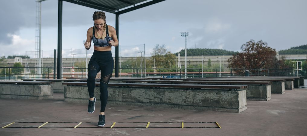 Sportswoman jumping on an agility ladder