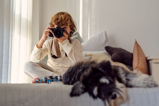 Unrecognizable boy taking photo on camera against fluffy dog ind