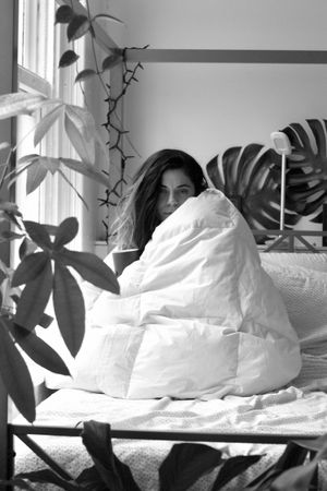Grayscale photo of woman covered with blanket sitting on bed