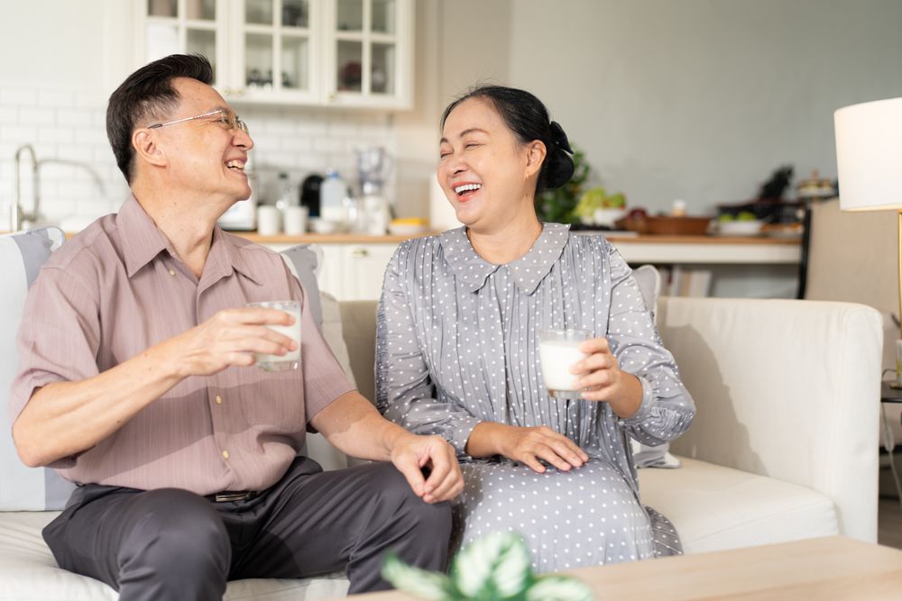 Happy Asian couple holding glass of milk and drinking together