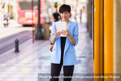 Woman in glasses and blue blazer standing on street looking at digital tablet bGRvYa
