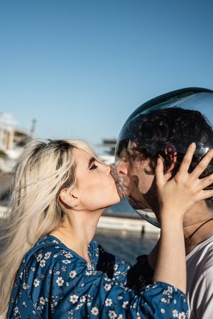 Adult woman touching fish bowl on head of tranquil boyfriend and showing tongue