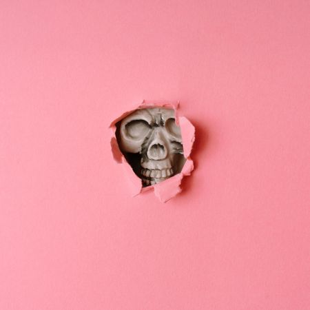 Skull breaking through pastel pink wall
