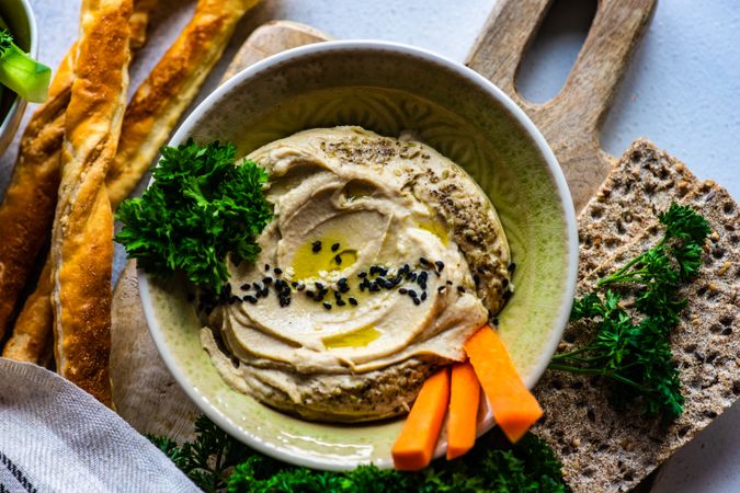 Top view of hummus dip in bowl on board served with veggies and rye crackers