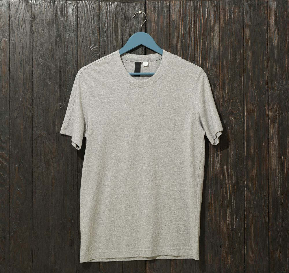 Hanger with blank gray t-shirt on wooden background, space for text