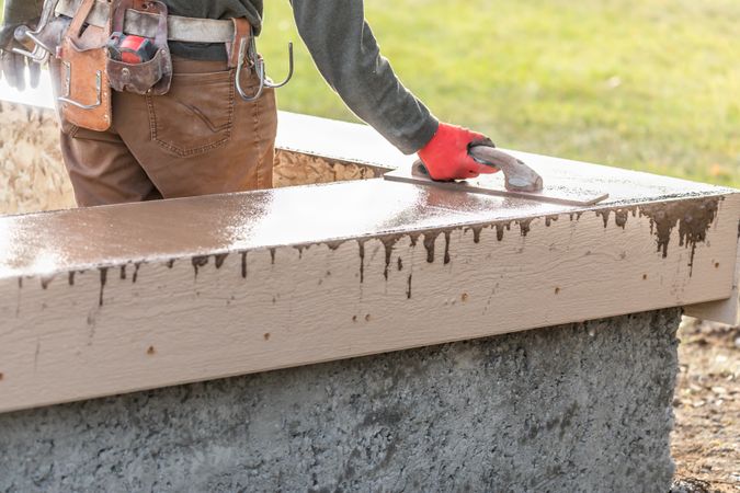 Construction Worker Using Wood Trowel On Wet Cement Forming Coping Around New Pool