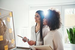 Two colleagues consult sticky notes on a board