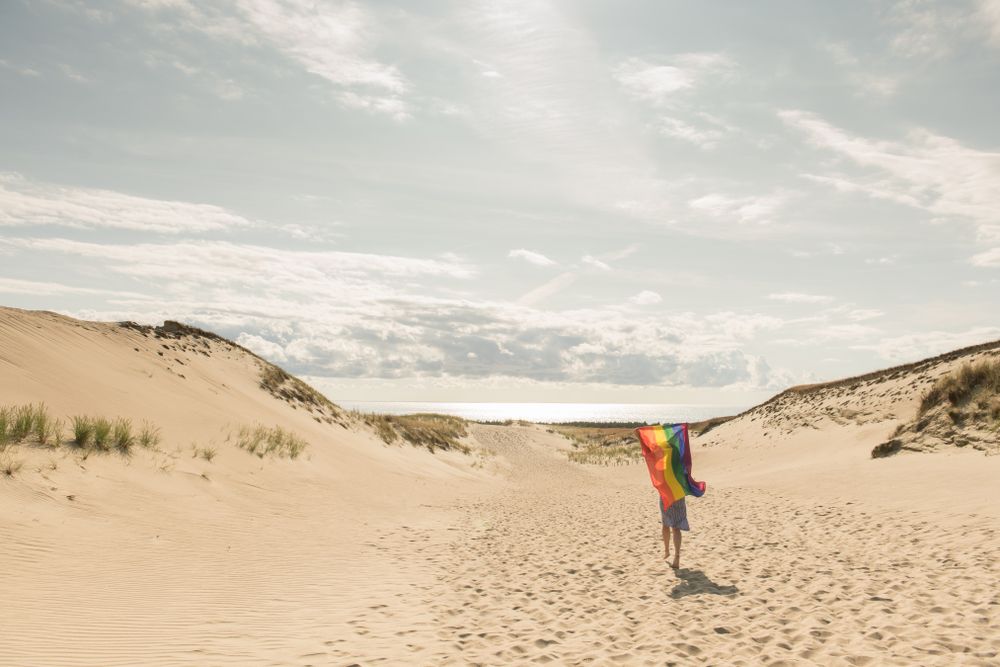 Young woman with rainbow banner against sky
