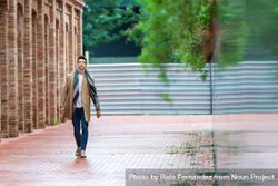 Portrait of young man in open fall coat walking down brick road 56G2zL