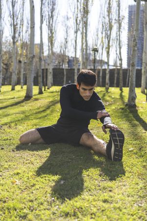 Sporty man stretching legs after working out in city public park