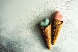 Two ceramic hearts in waffle cones on grey background with glitter and space for text