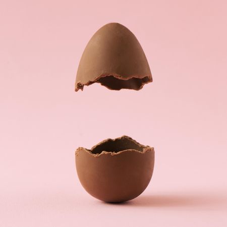 Chocolate Easter egg broken in half on pastel pink background with creative copy space