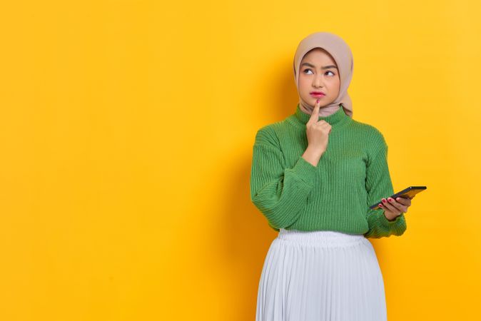 Woman in headscarf holding smart phone with finger on chin